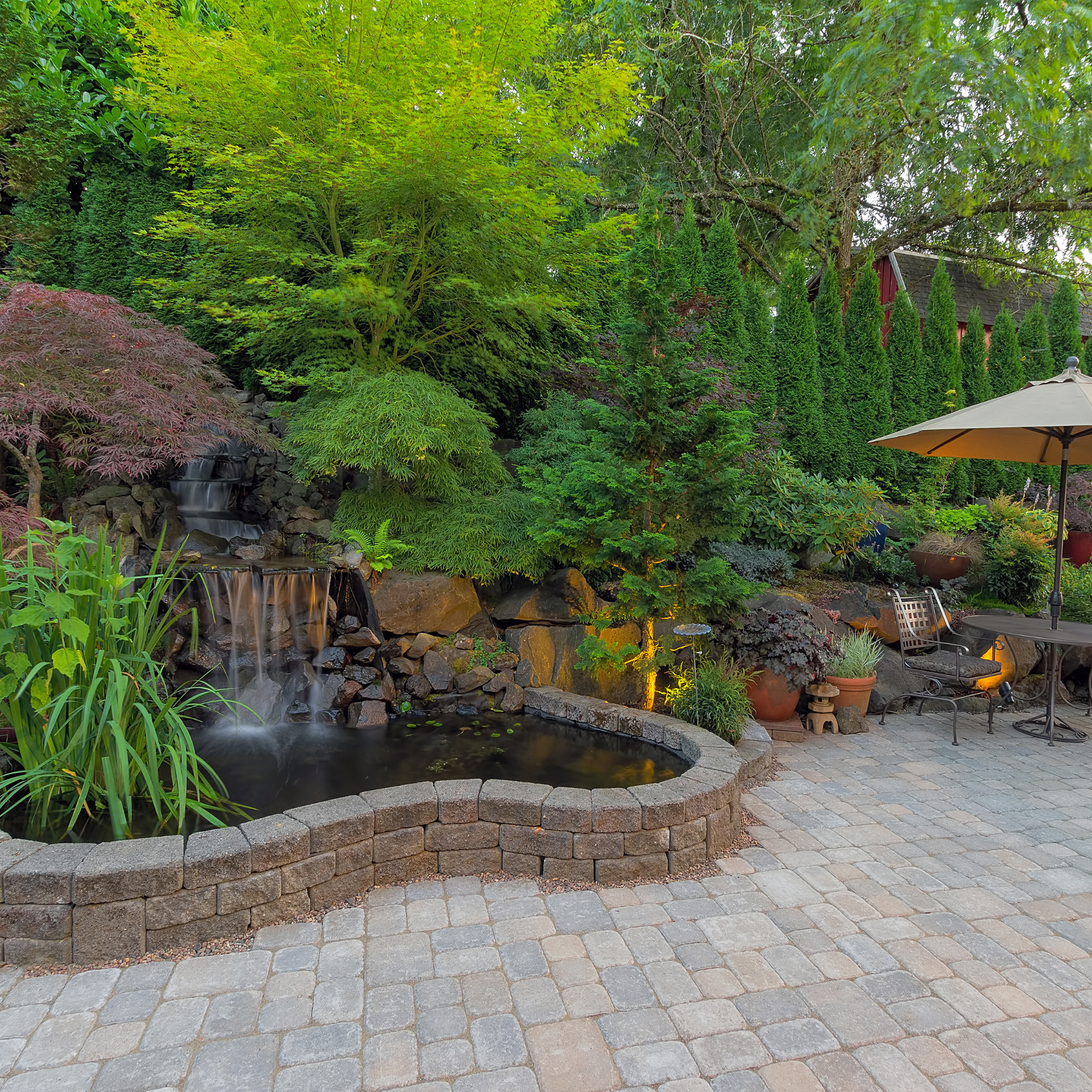 Custom stone patio with seating area, water feature, and landscape lighting designed by Willamette Valley Landscape in Salem, Oregon.